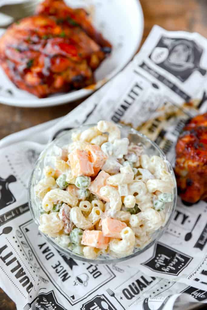 pasta salad in a small glass bowl on newsprint paper with BBQ chicken.