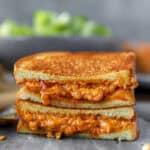 two pieces of pimento cheese grilled cheese stacked on top of either other on a grey stone platter.