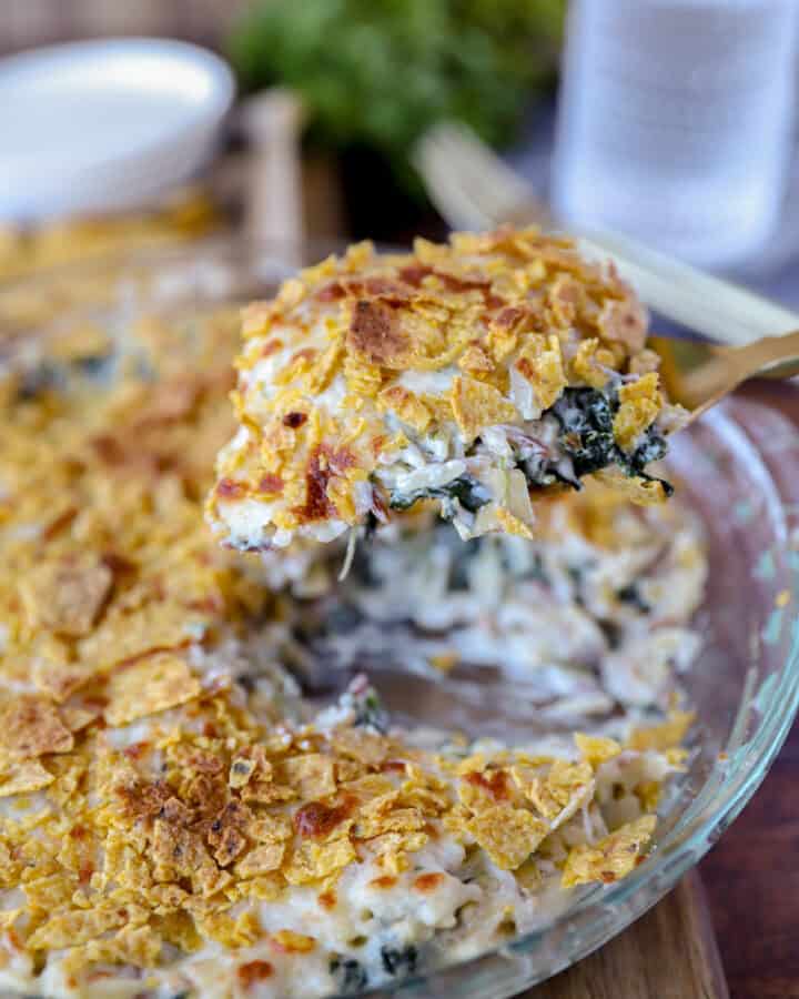 a large gold spoon scooping the spinach dip pasta from a glass pie dish.