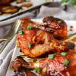 baked BBQ chicken drumsticks on a white platter with a gold serving spoon.