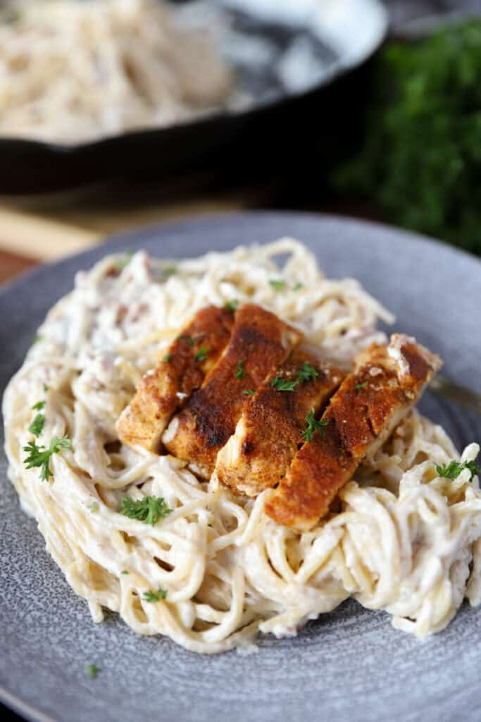 sliced cooked chicken on a bed of the creamy pasta noodles on a grey plate.
