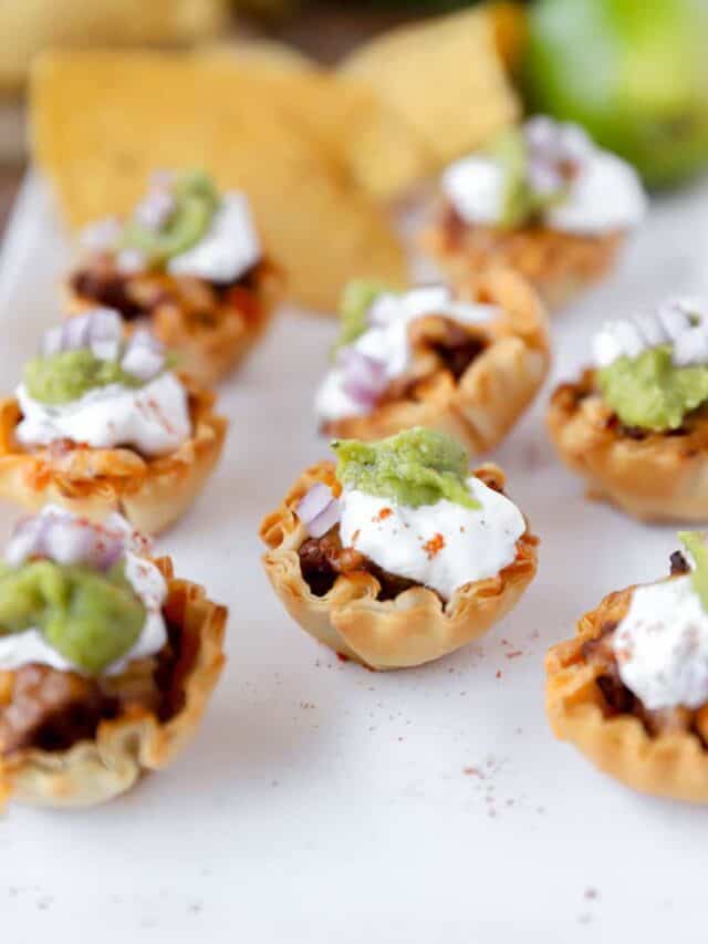 taco bites in phyllo cups on a white platter with tortilla chips and a lime in the background.