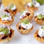 taco bites in phyllo cups on a white platter with tortilla chips and a lime in the background.