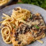 chicken marsala with fettucine noodles on a grey plate. Parsley in the background.