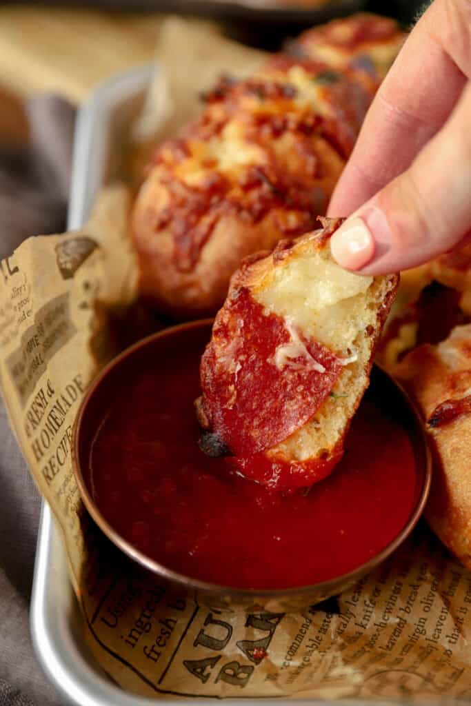 hand holding a piece of the pepperoni bread dipping it into a copper dish of marinata sauce.