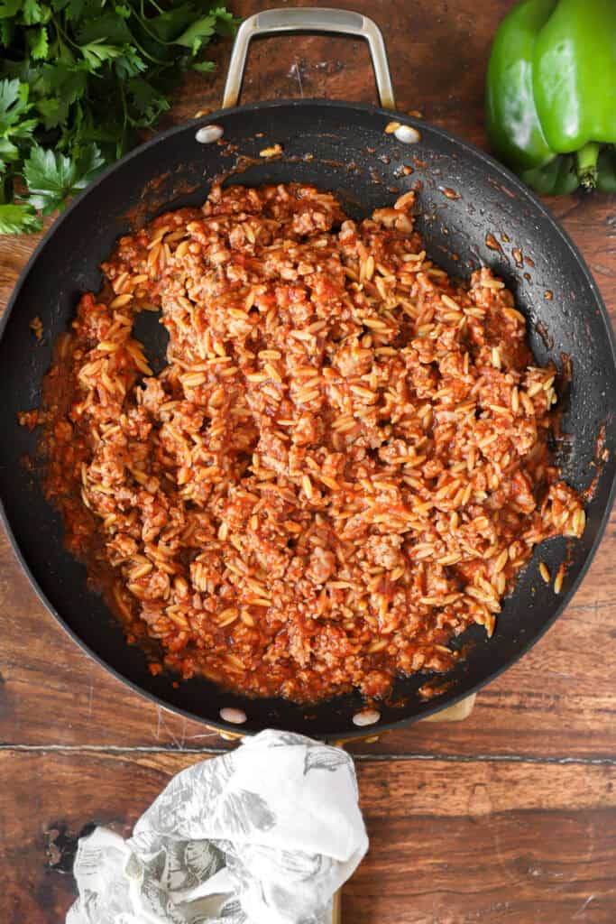 overhead photo of the sausage orzo mixture in a dark nonstick pan on a wood surface.