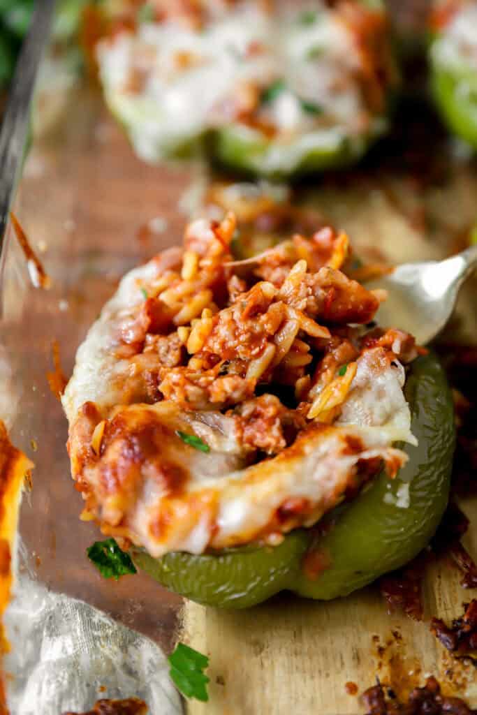 fork scooping the sausage orzo filling from a green bell pepper stuffed pepper.