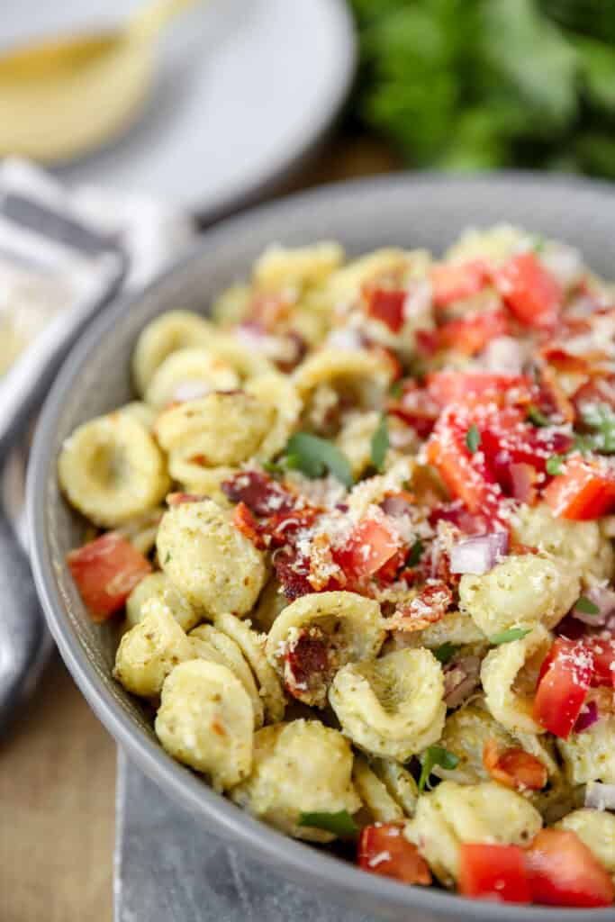 close view of the bacon pesto pasta in a grey round bowl with parsley blurred in the background.