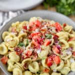 bacon pesto pasta topped with red onions and tomatoes in a grey round bowl.