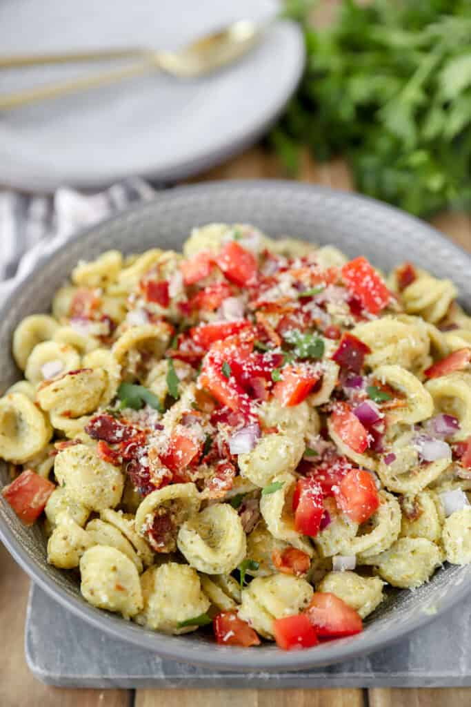 bacon pesto pasta topped with red onions and tomatoes in a grey round bowl.