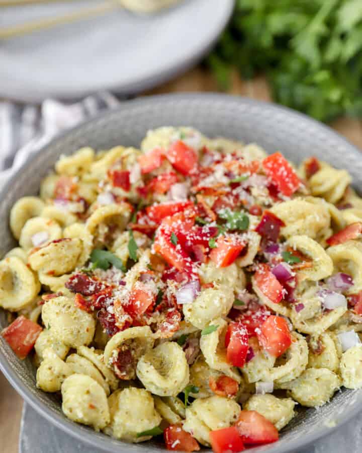 bacon pesto pasta topped with red onions and tomatoes in a grey round bowl.