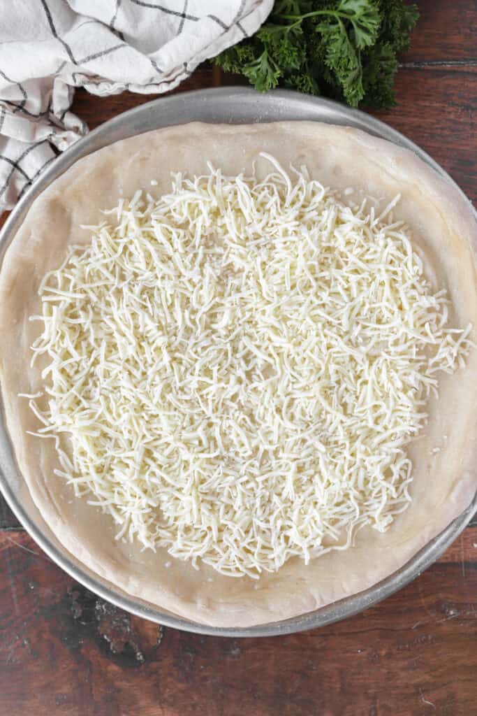 side by side two photos. Left photo shows the plain baked pizza dough. Right photo shows the dough now topped with the shredded Mozzarella cheese.