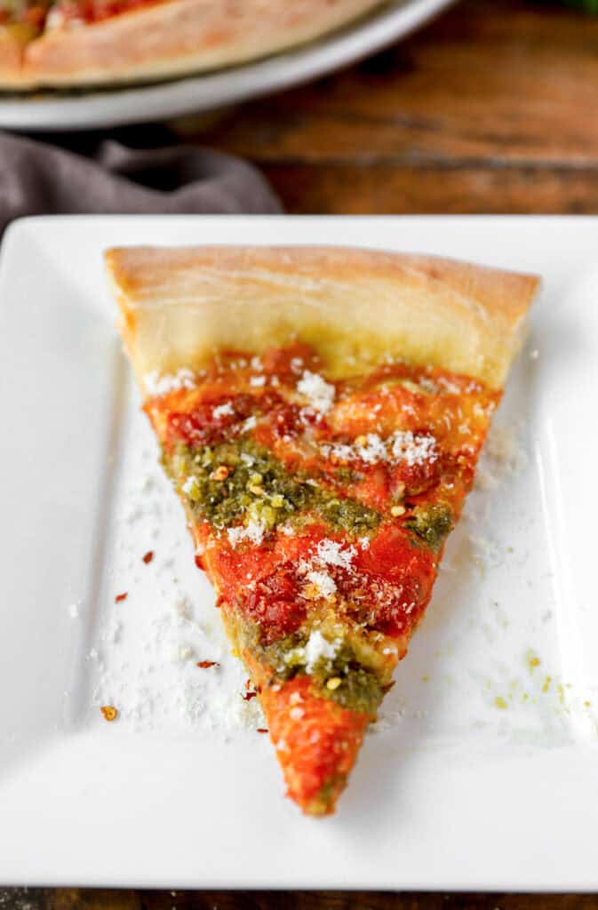 one slice of pizza topped with grated cheese and crushed red pepper flakes on a square white plate.