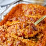 a gold spoon scooping the salsa chicken casserole dish with cooked rice. Tortilla chips, limes, and plates blurred in the background.