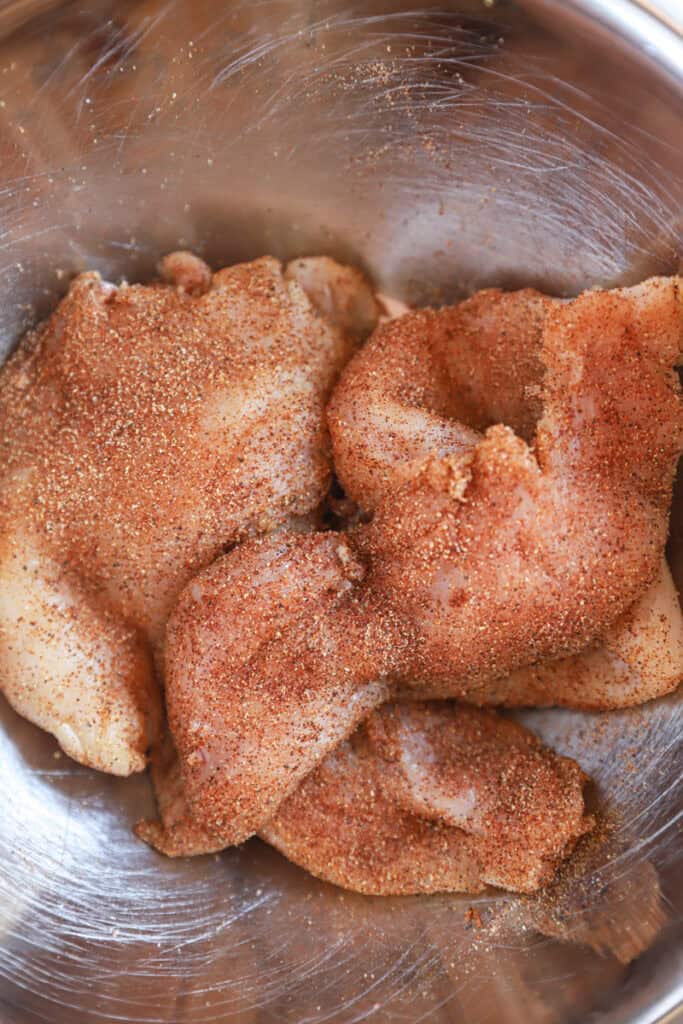 side by side two photos. Left photo is the spices in a small copper dish on a wood stone trivet. Right photo is the seasoned chicken in a stainless steel bowl.