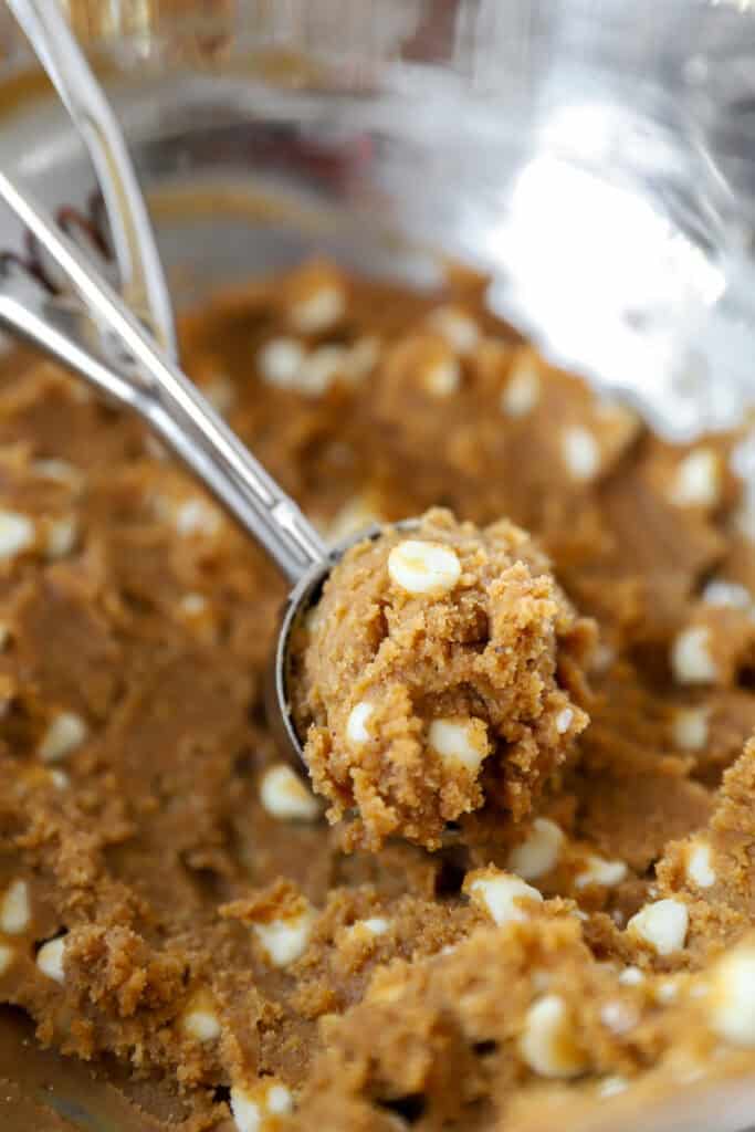 a scooper filled with the pumpkin cookie dough sitting in the bowl of the dough.