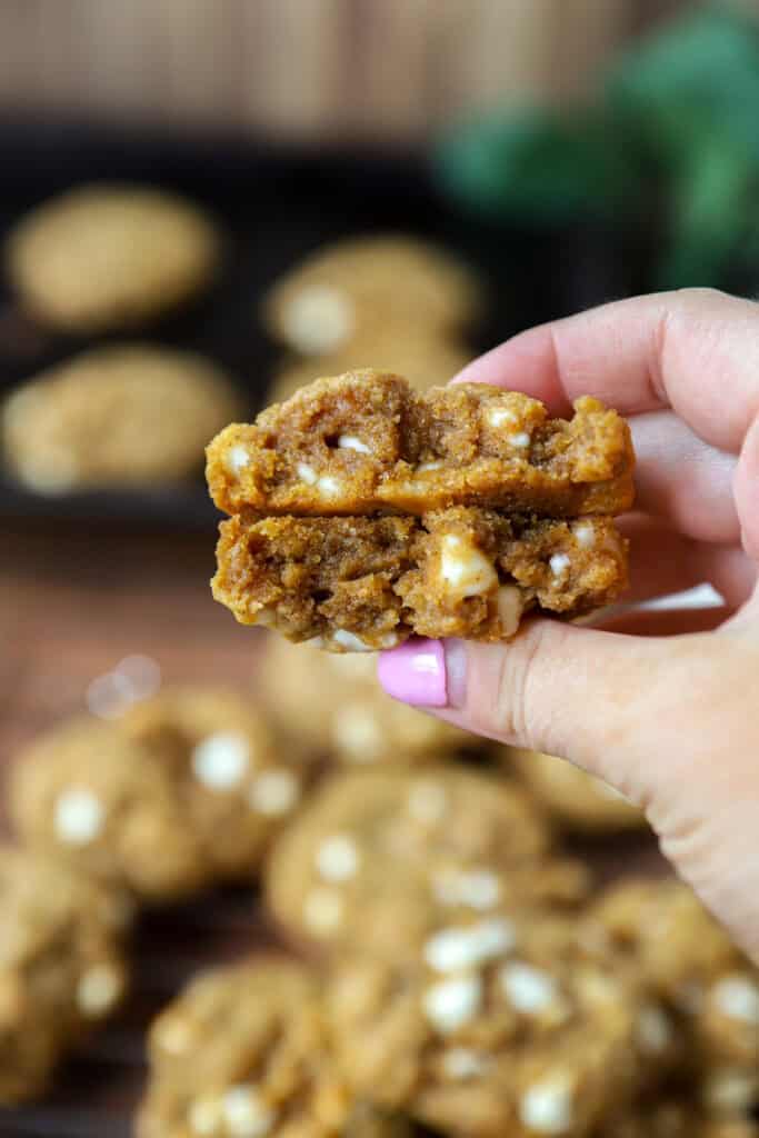 a hand holding one of the cookies that's been broken in half to show the inside texture. The remaining cookies on the cooling rack blurred in the background.