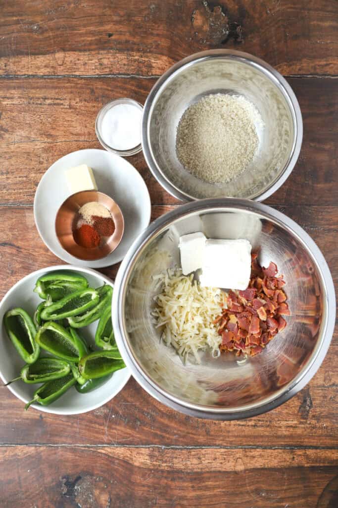 overhead flat lay photo of the ingredients on a dark wood surface: panko, salt, seasonings, butter, jalapeno peppers, cream cheese, bacon crumbles, shredded pepper jack cheese.