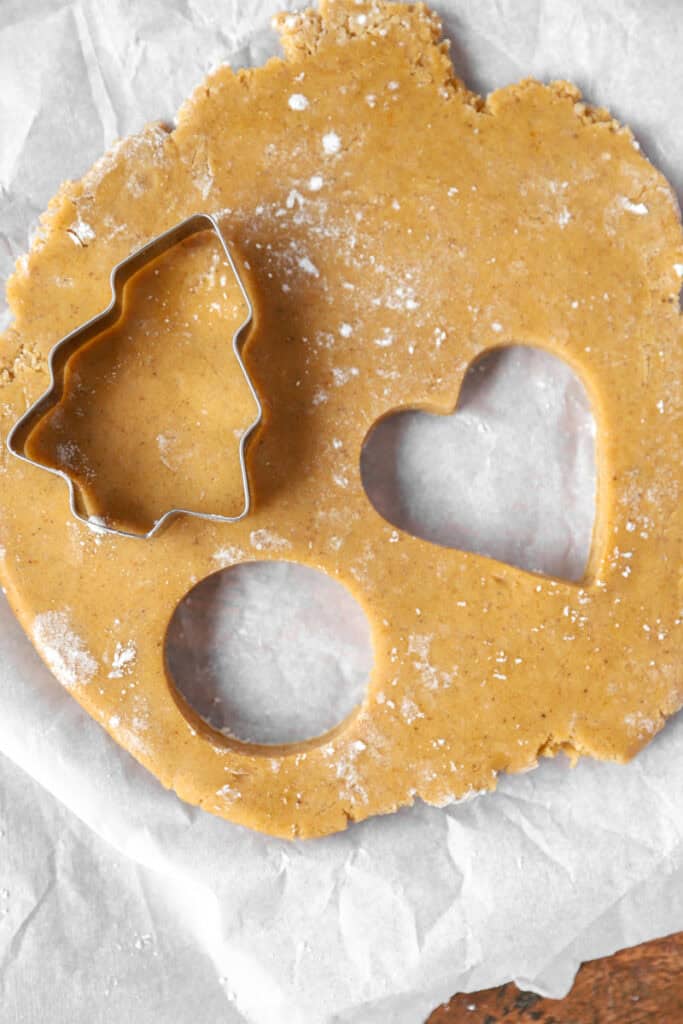 overhead photo of the rolled cookie dough on parchment paper with cookie cutter shapes cut out.