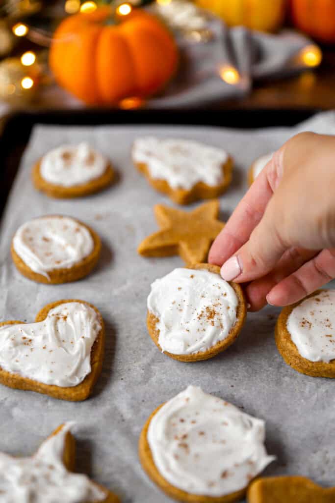 a hand picking up one of the frosted cookies from the baking sheet.
