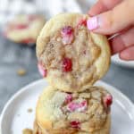 a hand holding one of the strawberry and cream cookies over a stack of cookies on a round white plate.