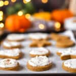 baked and frosted pumpkin sugar cookies on a parchment paper lined baking sheet. Blurred white string lights and pumpkins in the background.