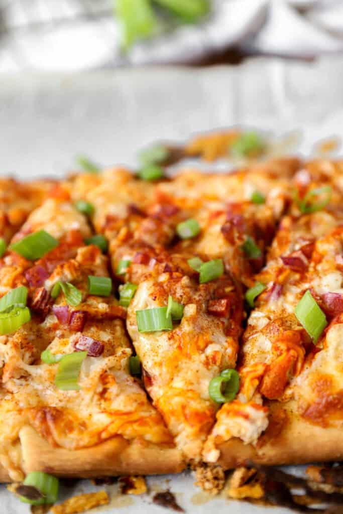 Buffalo chicken flatbread sliced and topped with diced scallions.
