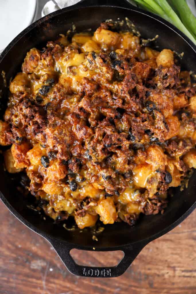 overhead view of the baked totchos layered with the beans, ground beef, and Cheddar cheese in a cast iron skillet