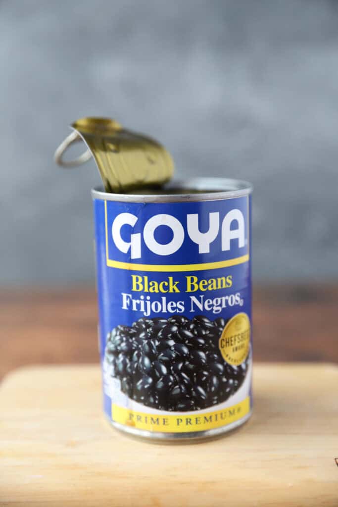 an open can of black beans on a wood board.