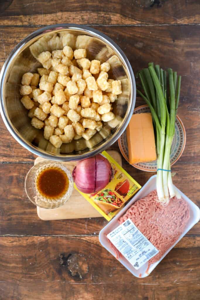 overhead photo of the ingredients: tater tots, seasonings mixed with oil, red onion, taco seasoning, Cheddar cheese, scallions, ground beef.