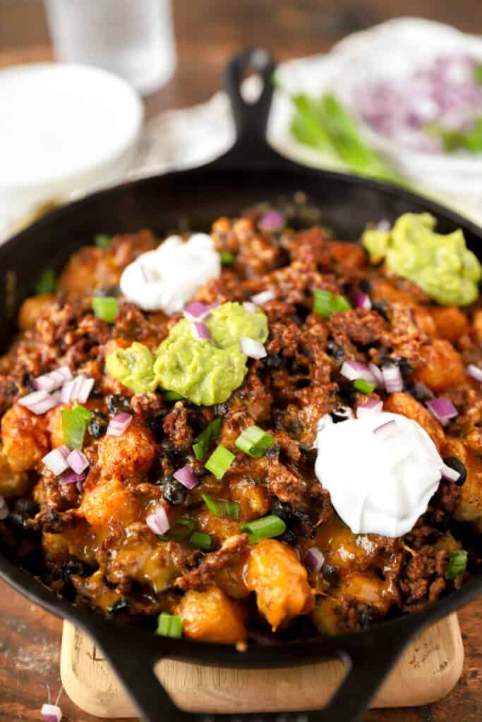 baked totchos topped with guac, sour cream, scallions, and red onions in a cast iron skillet.