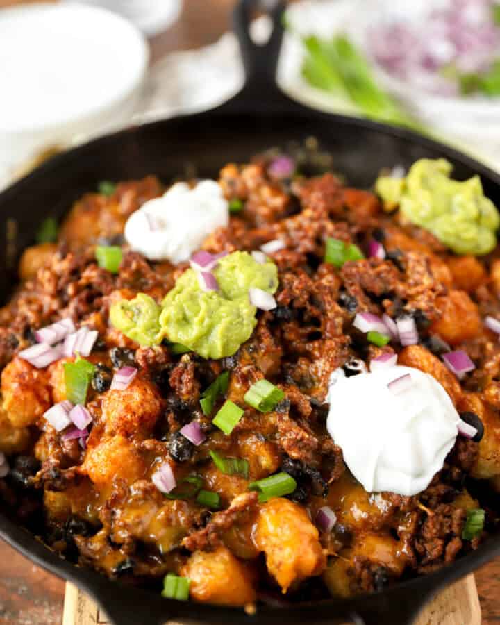 baked totchos topped with guac, sour cream, scallions, and red onions in a cast iron skillet.