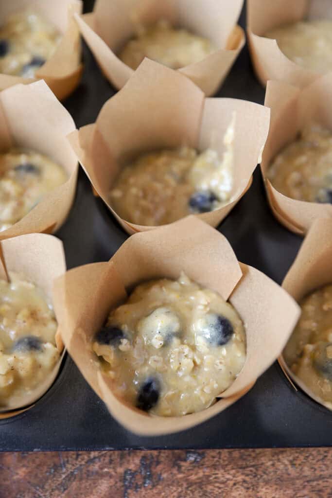 the banana blueberry oat muffin batter in the brown muffin liners in the muffin tin.