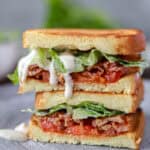 Two pieces Caesar BLT sandwich stacked on top of each other on a grey round plate. Caesar dressing is dripping from the top piece.