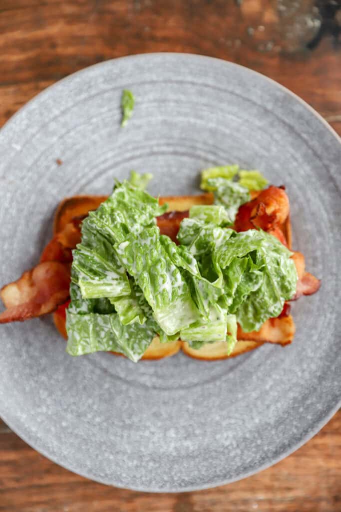 overhead photo of the Caesar chopped romaine added on top of the sandwich on a round grey plate.