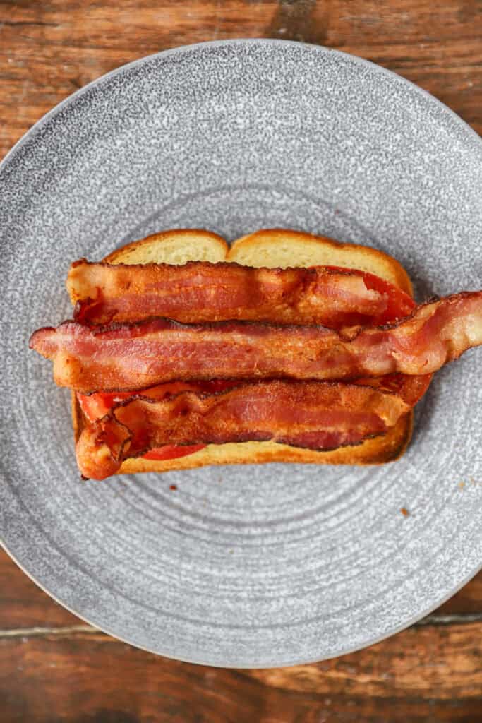 overhead photo of the bacon added on top of the sandwich on a round grey plate.