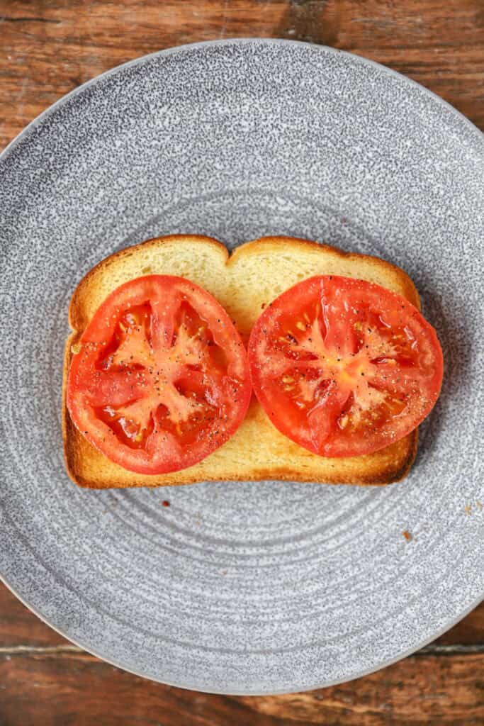 overhead photo of the tomato slices on the piece of toast on a round grey plate.