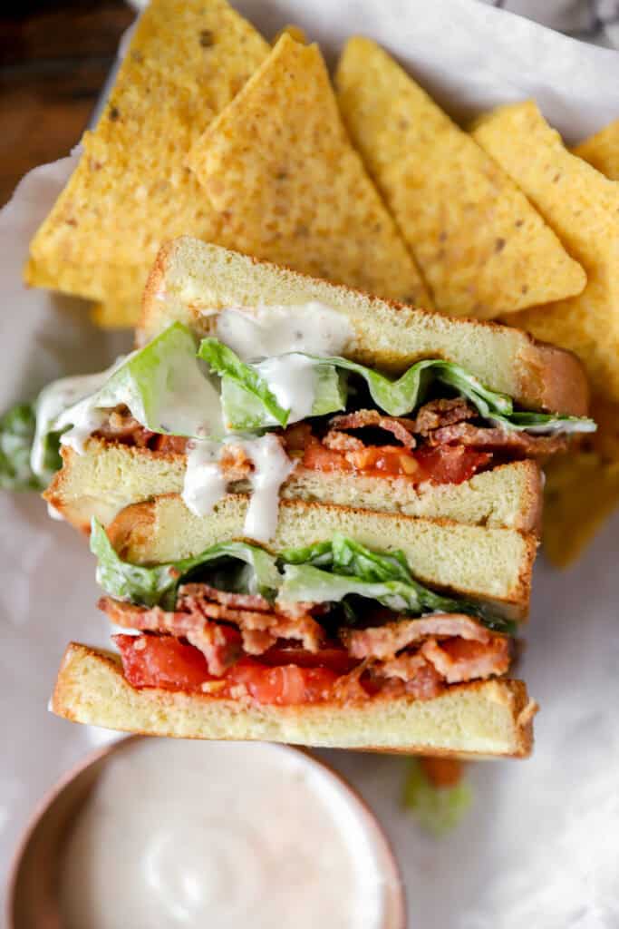 overhead photo of the Caesar BLT with tortilla chips on white parchment paper with a small copper dish with Caesar dressing.