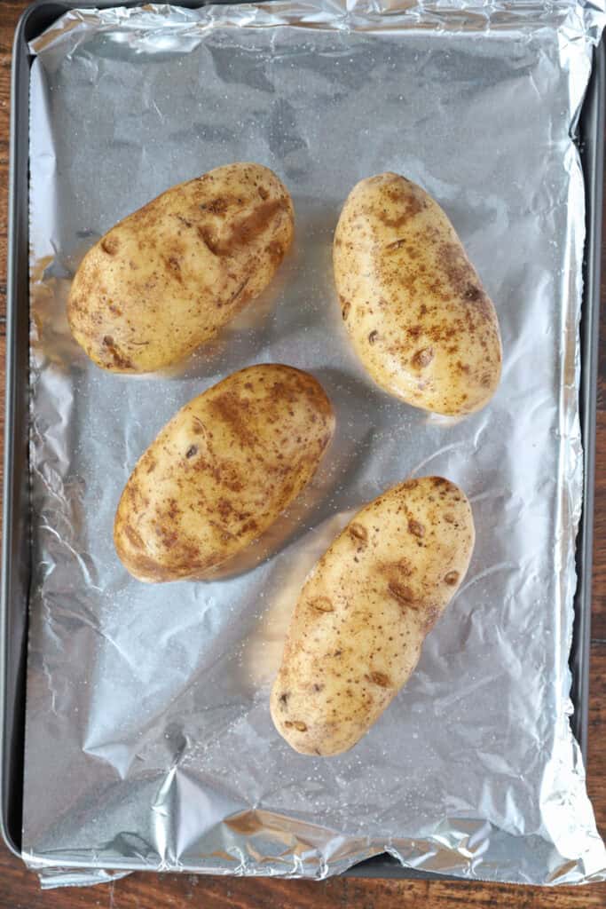 overhead photo of baked potatoes on a foil lined baking sheet.