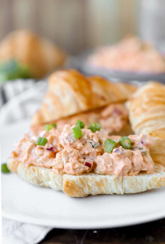 Buffalo chicken chicken salad on a croissant topped with diced scallions on a white plate.