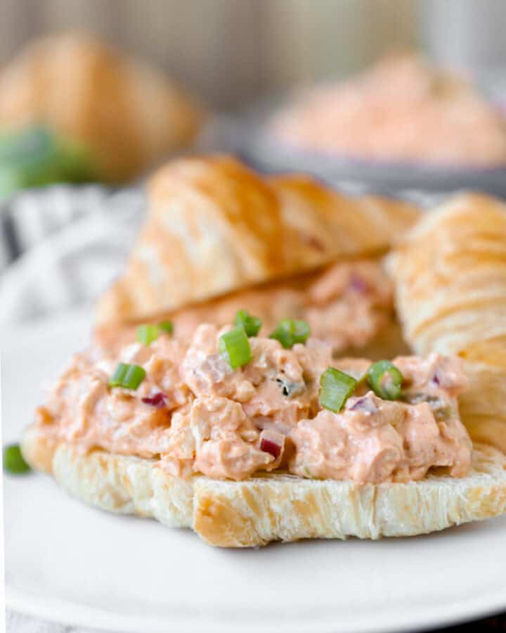 Buffalo chicken chicken salad on a croissant topped with diced scallions on a white plate.