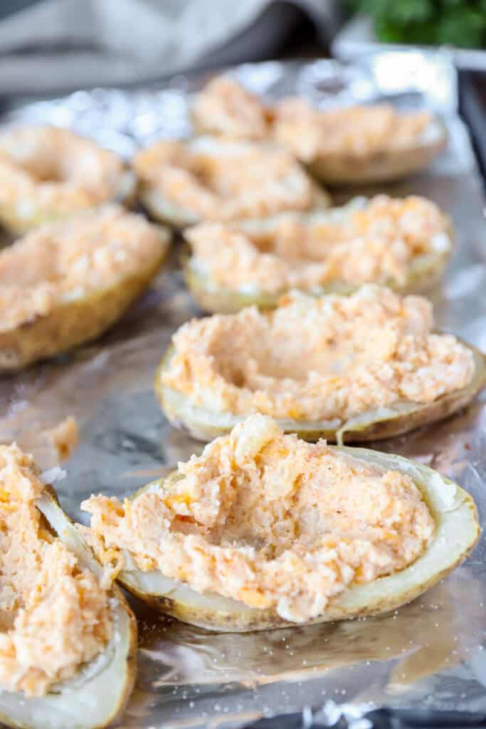 The potato skin shells now filled with the cheesy center on a foil lined baking sheet.