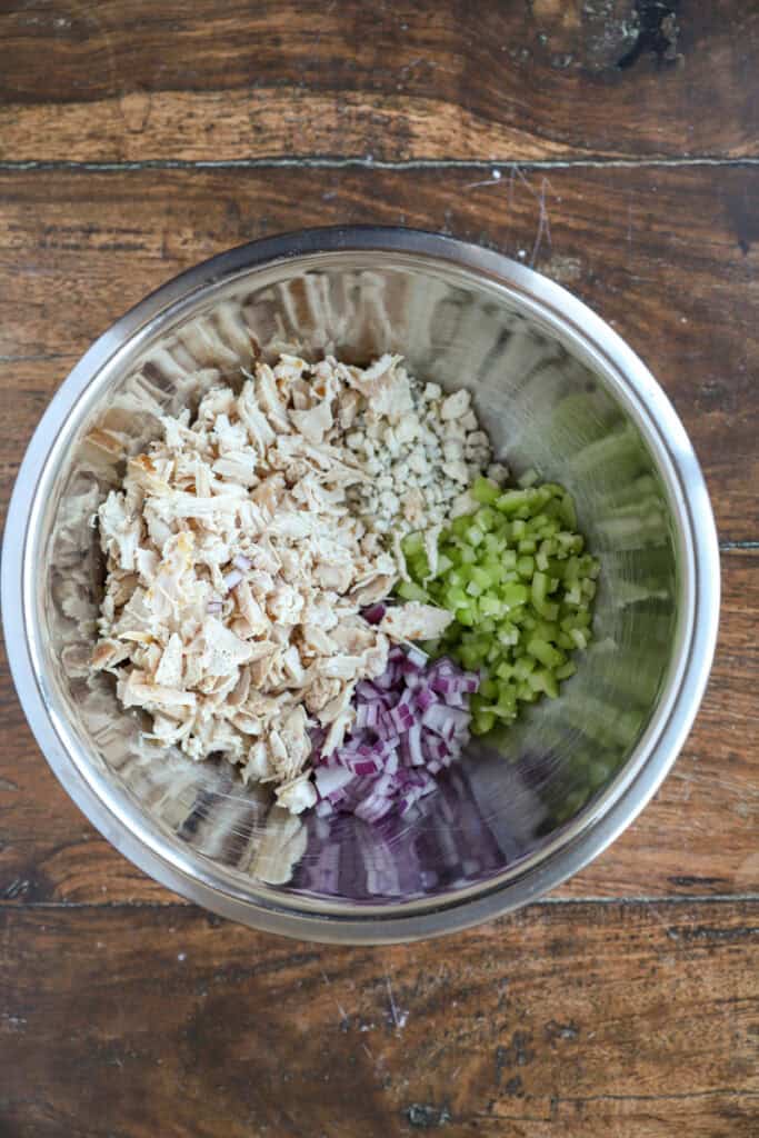 overhead photo of the ingredients in a stainless steel bowl: shredded chicken, diced celery, crumbled blue cheese, diced red onions.