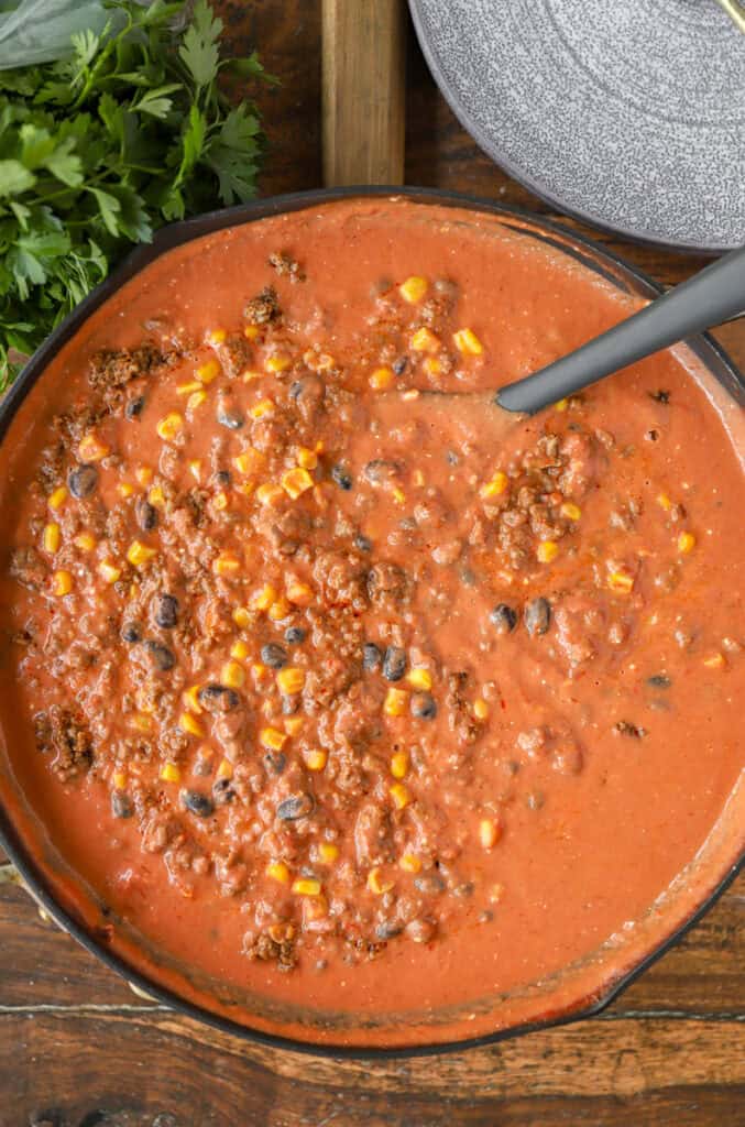 overhead photo of the taco ground beef sauce in a nonstick pan with a black spoon.