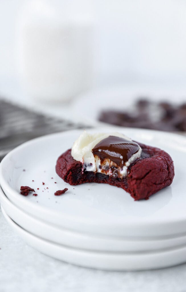 one bitten red velvet cookie on a stack of 3 round white plates.