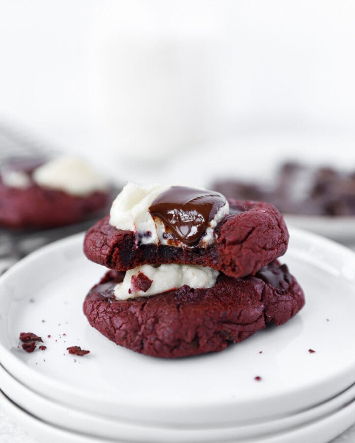 stack of 2 red velvet cookies on round white plates.