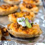 A spatula lifting one taco twice baked potato from a foil lined baking sheet.