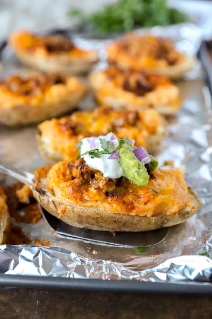 A spatula lifting one taco twice baked potato from a foil lined baking sheet.