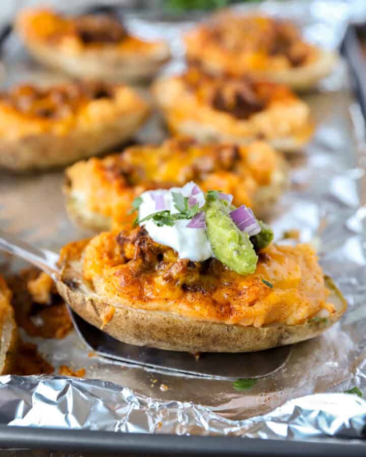 A spatula lifting one taco twice baked potato from a foil lined baking sheet.