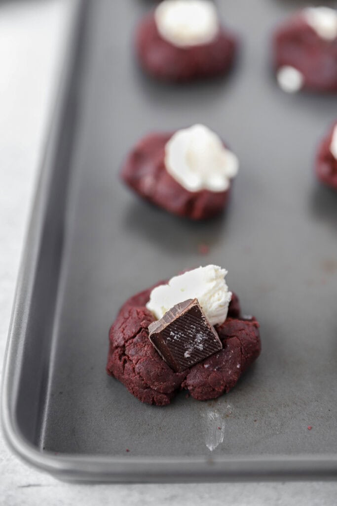 the unbaked cookies on the cookie sheet topped with the cream cheese and square of dark chocolate.